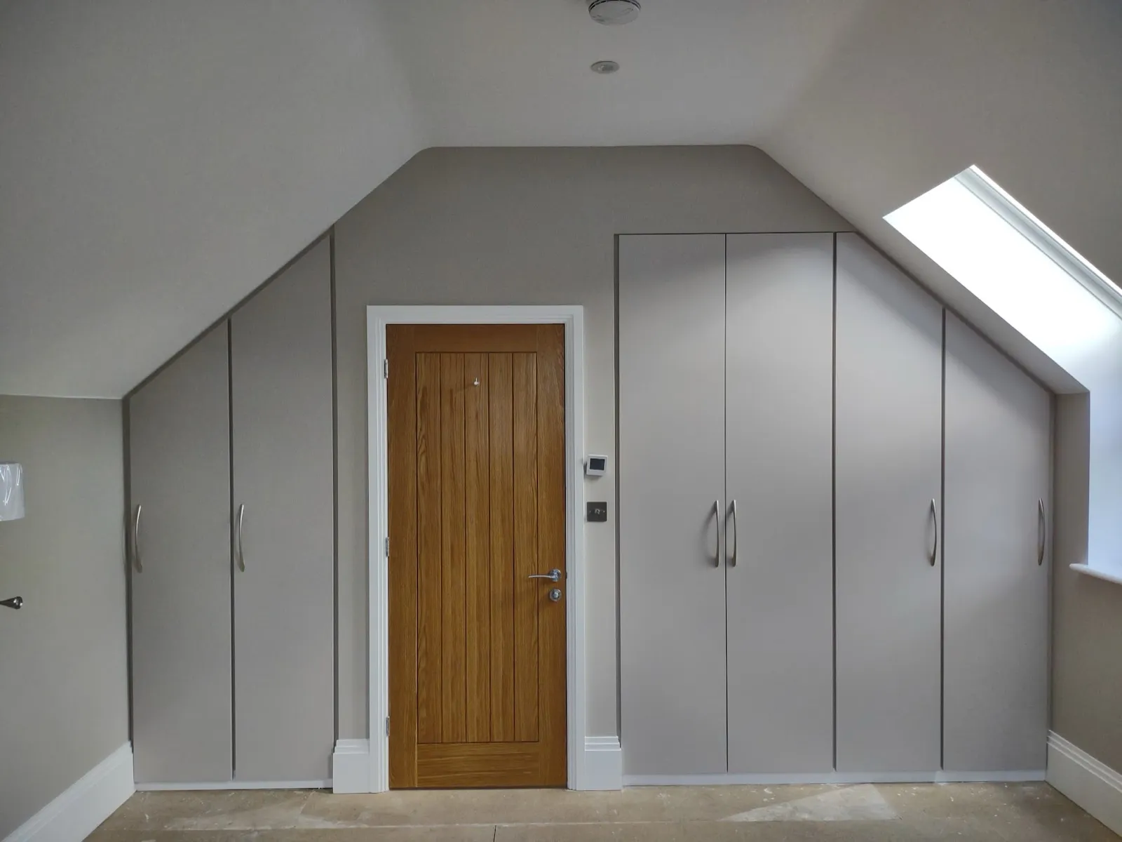 Grey fitted wardrobes built into a sloped-ceiling loft bedroom, South London