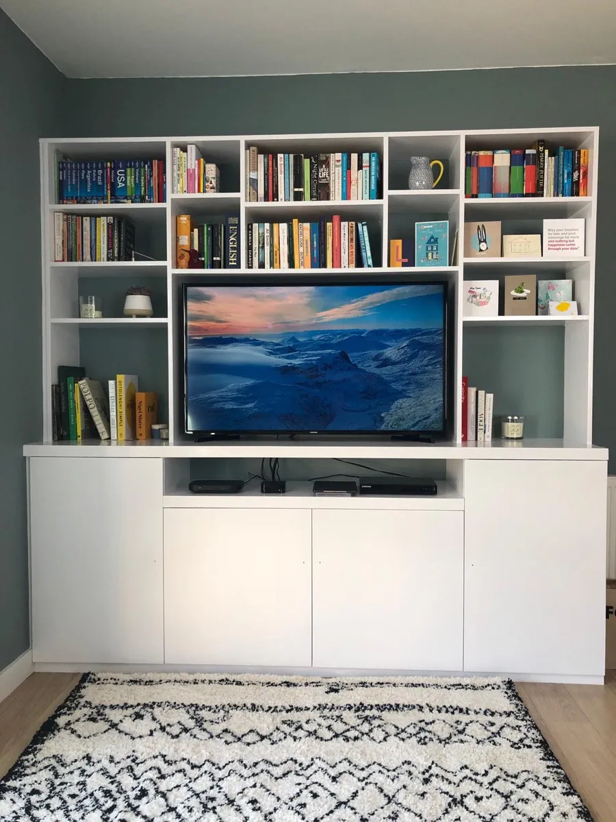 White fitted media wall with shelving and TV unit in a sage-green living room